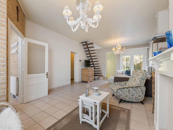 A spacious living area with a staircase, a white sofa, a small table, and a chandelier. - Comfortable house in the heart of the village (Le Bizet)