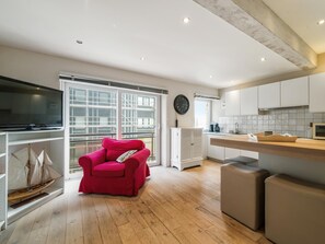Een moderne keuken met houten vloer, een rode stoel, een flatscreen televisie en een groot raam met uitzicht op steigers.
