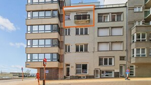 Ein mehrgeschossiges Gebäude mit einer flachen Fassade, großen Fenstern und einem Parkplatz mit einem Verbotsschild.