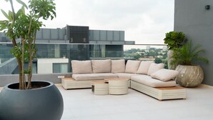 Un espacio al aire libre moderno con un sofá modular, dos mesas auxiliares y una maceta grande con un árbol.