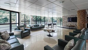 En rummelig lobby med et moderne design, der inkluderer et siddeområde med sofaer og lænestole, et centralt sofabord og et stort vindue med udsigt til det fri.