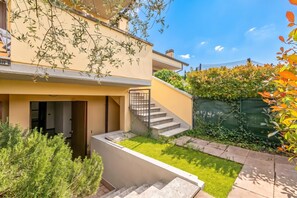 A modern two-story building with a flat roof, a staircase leading to the upper floor, and a well-maintained garden area with grass and shrubs. - Juliette House: Shared Pool & Relax (Salò)