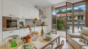 A modern kitchen with white cabinets, stainless steel appliances, and a dining area with a table set for two. - Juliette House: Shared Pool & Relax (Salò)