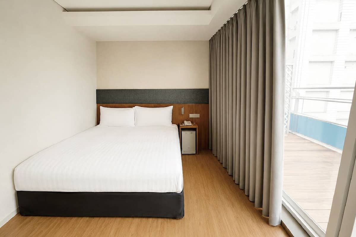 A hotel room with a bed, a nightstand, a telephone, and a view of the outside.