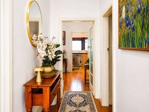 A hallway with a wooden console table, a mirror, a vase of flowers, and a rug leading to a kitchen area. - Spacious 4-Bed Retreat in Vibrant Footscray (Footscray)