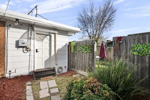 A residential property with a white door, a mailbox, a small step leading to the door, a wooden fence with greenery, and a clear sky. - Spacious 4-Bed Retreat in Vibrant Footscray (Footscray)