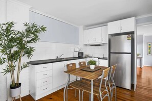 A modern kitchen with white cabinets, a stainless steel refrigerator, and a dining table with chairs. - Spacious 4-Bed Retreat in Vibrant Footscray (Footscray)