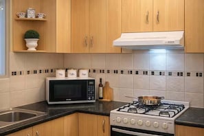 A kitchen with wooden cabinets, a microwave, a stove, and a sink. - Spacious 4-Bed Retreat in Vibrant Footscray (Footscray)