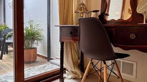 Et værelse med skrivebord, stol, spejl, lampe og en potteplante.