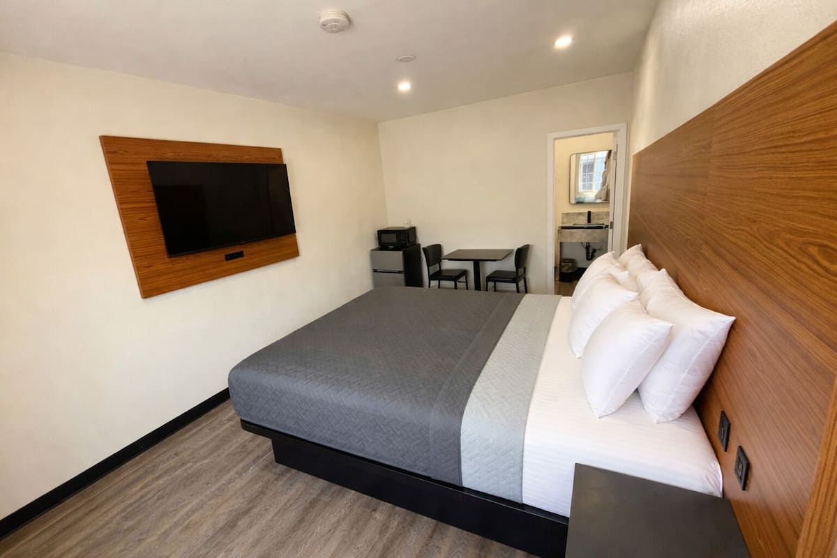 A hotel room with a bed, a TV mounted on the wall, a desk with a chair, and a microwave.