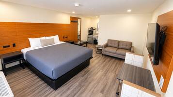 Una habitación de hotel moderna con una cama grande, un sofá, una mesita, un televisor y una kitchenette.