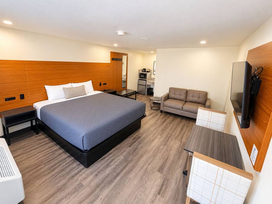 Una habitación de hotel moderna con una cama grande, un sofá, una mesita, un televisor y una kitchenette.