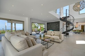 A spacious living area with a large sofa, a coffee table, and a spiral staircase. - Villa Amantos - Denia, Costa Blanca (Denia)