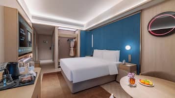 A hotel room with a bed, bedside table, TV, and a small dining area with a fruit plate.