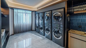 A modern laundry room with four stacked front-loading washing machines, a built-in sink, and a tiled backsplash. - Crystal Orange Shenzhen Bao'an Joy City (Shenzhen)