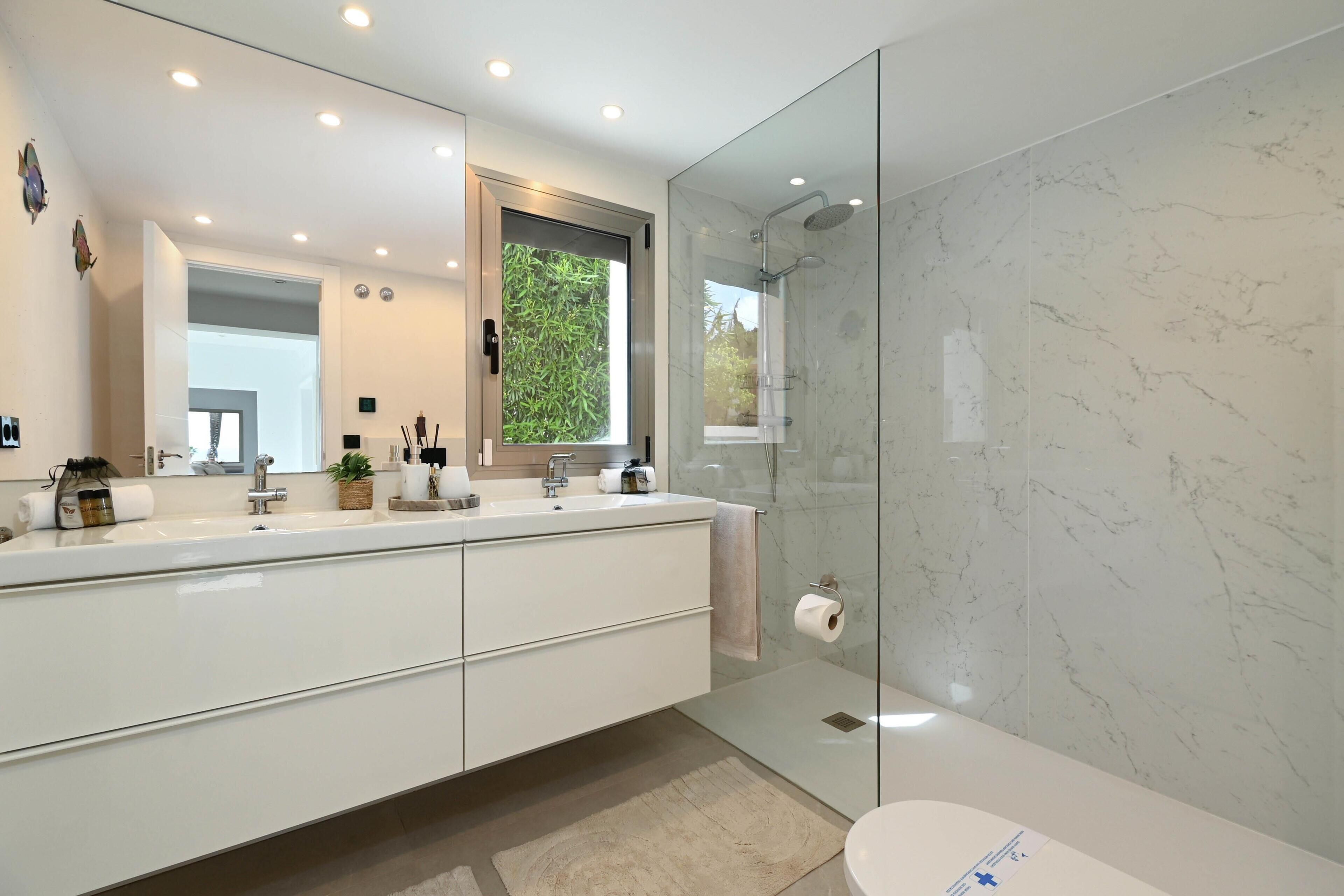 A modern bathroom with a large mirror, a glass shower enclosure, and a white sink.