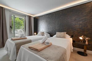 Ein Hotelzimmer mit zwei Betten, einem kleinen Tisch mit Lampe und Blick auf Grünfläche.