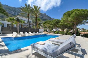 Ein Pool mit Liegestühlen, Palmen und einem Berg im Hintergrund.