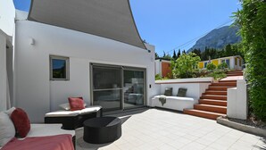 Eine moderne Außenpatio mit großem Sonnenschirm, einer Couch, einem Esstisch und einer Treppe, die zu einer zweiten Ebene führt.