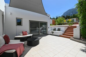 A modern outdoor patio with a large umbrella, a sofa, a dining table, and a staircase leading to a second level. - Villa Amantos 8 pax - Denia, Costa Blanca (Denia)