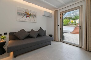 Een moderne woonkamer met een grijze bank, een kleurrijk abstract schilderij en uitzicht op een trap die naar buiten leidt.