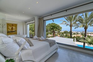 A bedroom with a large bed, a view of palm trees and the sea, and a poster on the wall. - Villa Amantos 8 pax - Denia, Costa Blanca (Denia)