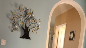 Una habitación con escritorio, silla, cuadro enmarcado y un árbol decorativo en la pared.