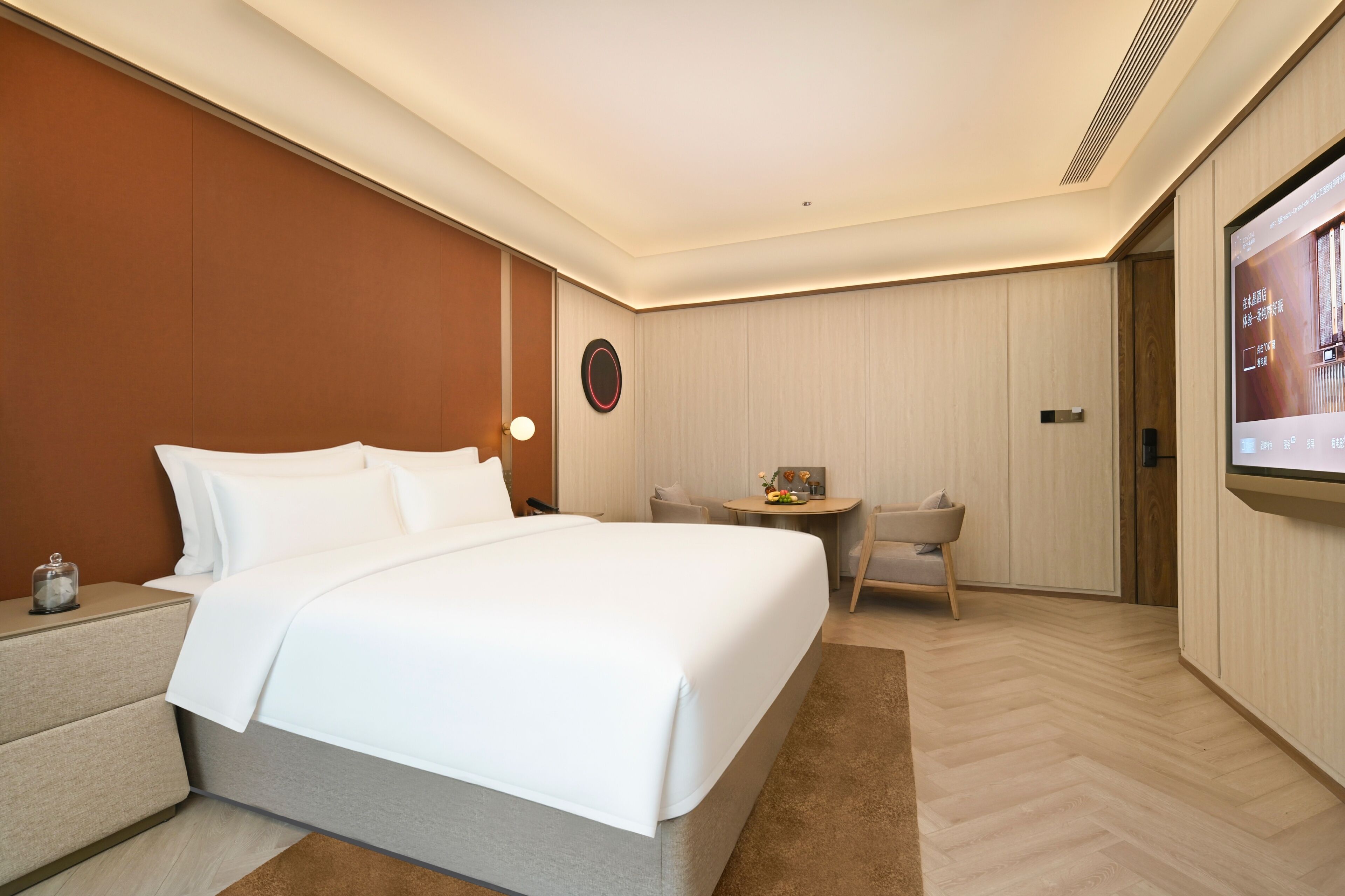 Une chambre d’hôtel avec un grand lit, une table de chevet, un petit bureau avec une chaise, un téléviseur fixé au mur et un plancher en bois.