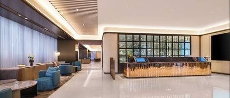 A modern hotel lobby with a reception desk, seating area, and a large window with a view.