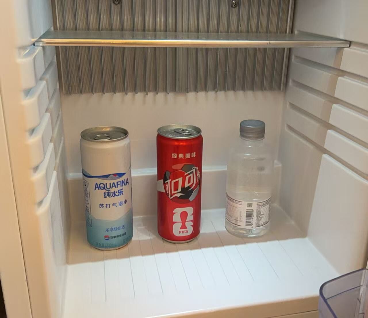 Un refrigerador con tres artículos: una lata de agua Aquafina, una lata de refresco Fifa y una botella de plástico transparente.