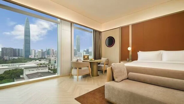 A hotel room with a large window, a bed, a desk, and a view of a cityscape. - Crystal Orange Hotel Shenzhen Futian (Shenzhen)