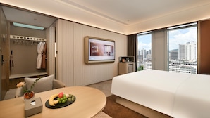 A hotel room with a bed, a TV, a desk with a fruit bowl, a bathroom with a robe, and a city view. - Crystal Orange Hotel Shenzhen Futian (Shenzhen)