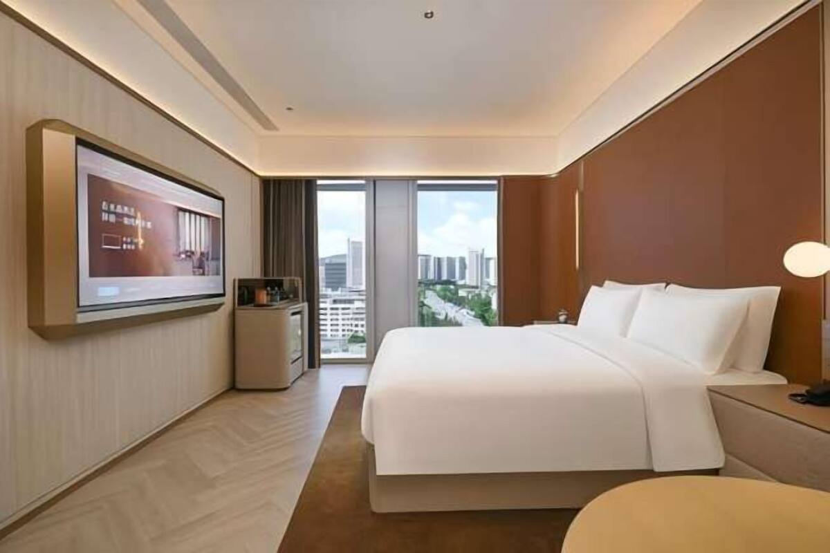 Quarto de hotel com uma cama grande, televisão na parede, uma mesinha e vista para a cidade.