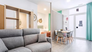 Una sala de estar moderna con un sofá gris, una zona de comedor con mesa y sillas, y una cocina al fondo.
