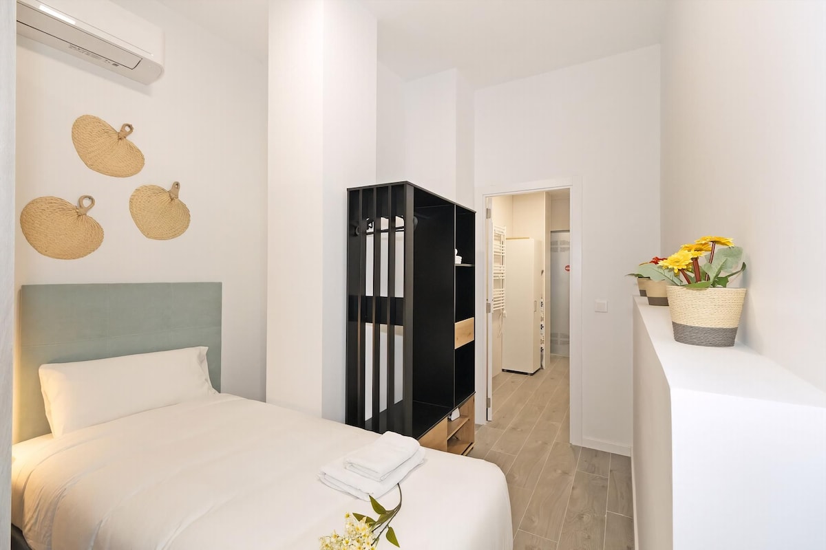 A hotel room with a bed, a wardrobe, a bathroom, and a small balcony with flowers.
