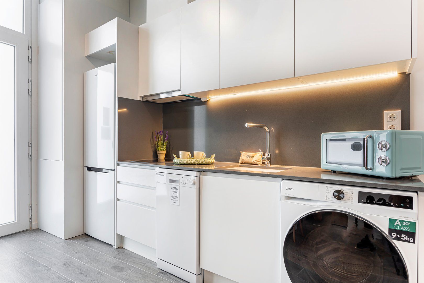 A modern kitchen with built-in appliances, a washing machine, and a toaster.