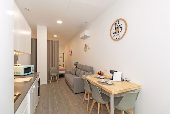 A modern kitchen with a microwave, a dining area with a wooden table and chairs, and a gray sofa. - Guestready - Fontilles Apartments (Valencia)