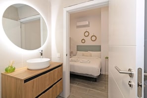 A modern bathroom with a round mirror, white sink, and wooden vanity. - Guestready - Fontilles Apartments (Valencia)