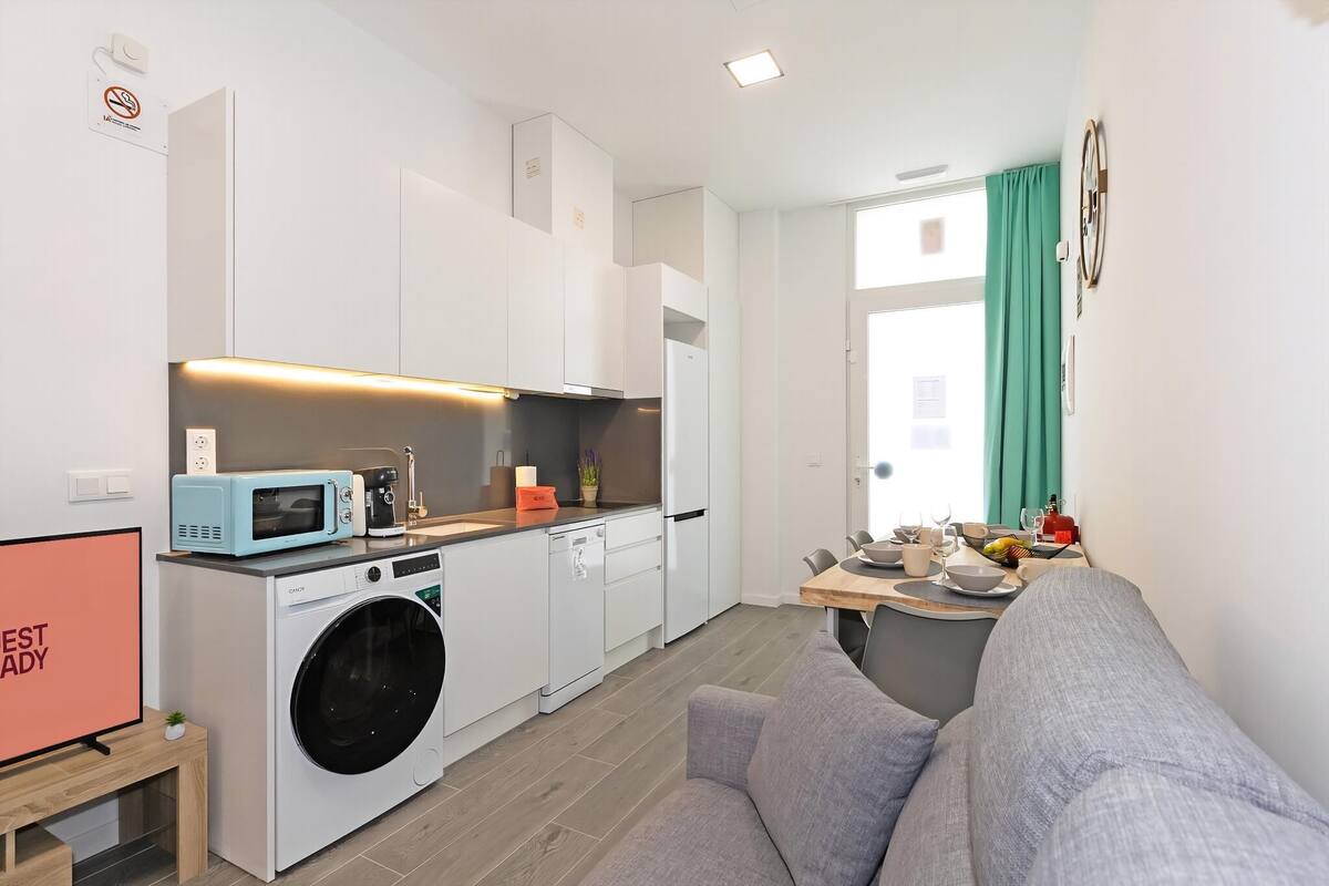A compact kitchen with a washing machine, microwave, and a dining area with a table and chairs.