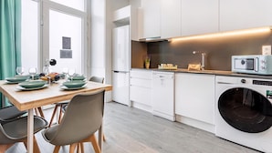 Una cocina moderna con armarios blancos, microondas integrado, lavadora y un comedor con mesa y sillas de madera.