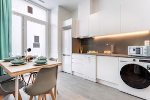 A modern kitchen with white cabinets, a built-in microwave, a washing machine, and a dining area with a wooden table and chairs. - Guestready - Fontilles Apartments (Valencia)