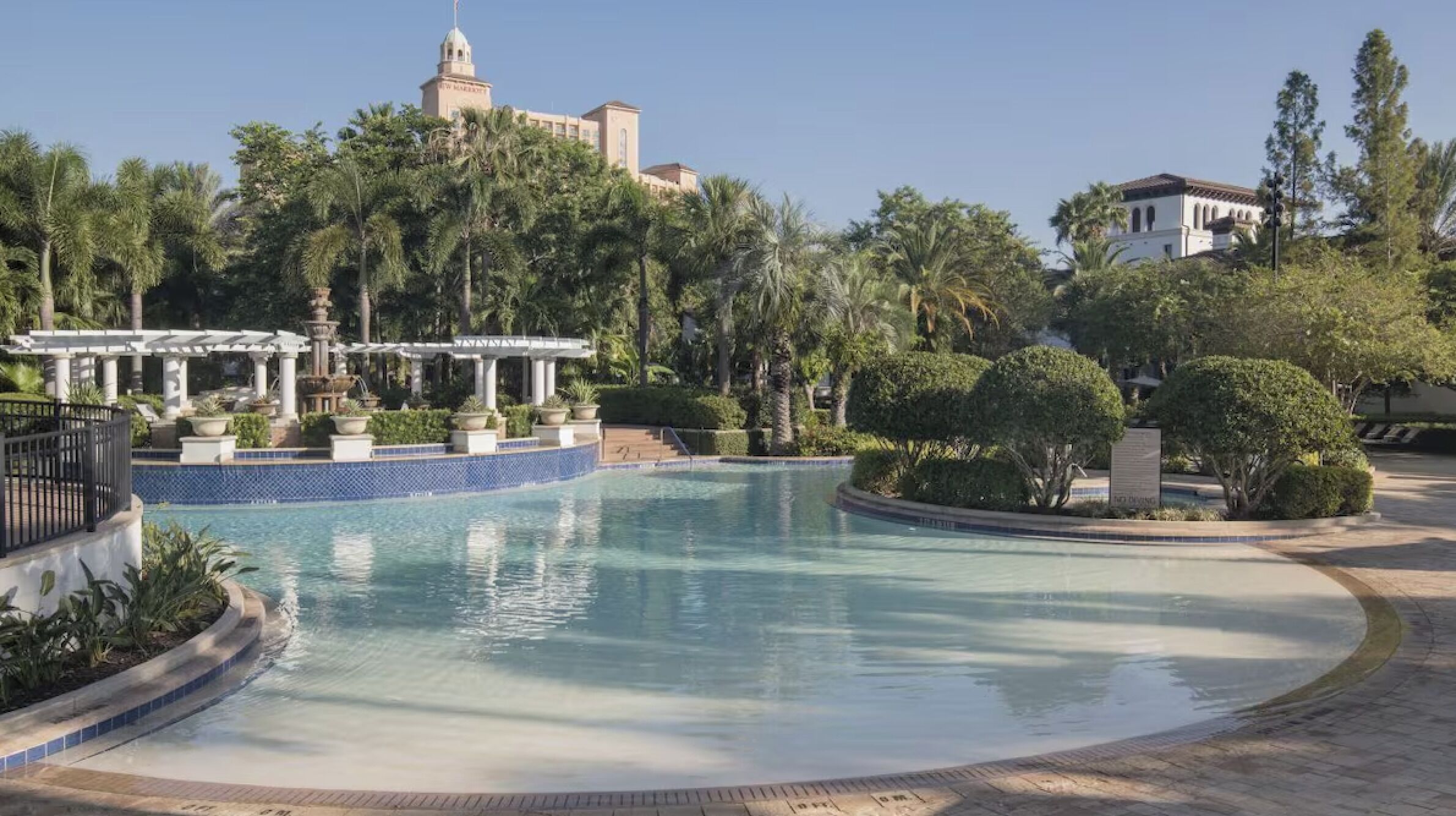 Una piscina con una pergola, palme e un edificio con una cupola sullo sfondo.