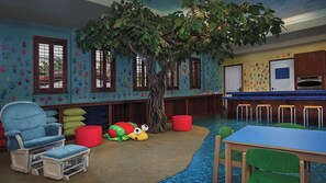 A playroom with a tree, colorful handprints on walls, a blue chair, a table, and a kitchen area.