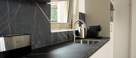 Una cocina moderna con encimera de mármol negro, pileta de acero inoxidable y una ventana sobre la pileta.