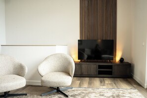 A modern living room with a flat-screen TV, two armchairs, a wooden entertainment unit, and a patterned rug. - With views over the water, within walking distance of the beach and close to the Veluwe  the perfect setting for nature, relaxation and outdoor activities. (Giesbeek)