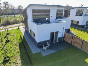 Een modern huis met twee verdiepingen, een plat dak, grote ramen en een terras met tuinmeubilair.