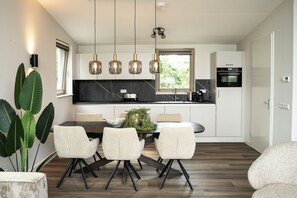 Een moderne keuken met een eettafel, stoelen, hanglampen en een koelkast.