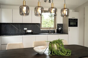 Una cocina moderna con lámparas colgantes, una ventana y un comedor con un tazón y una planta.