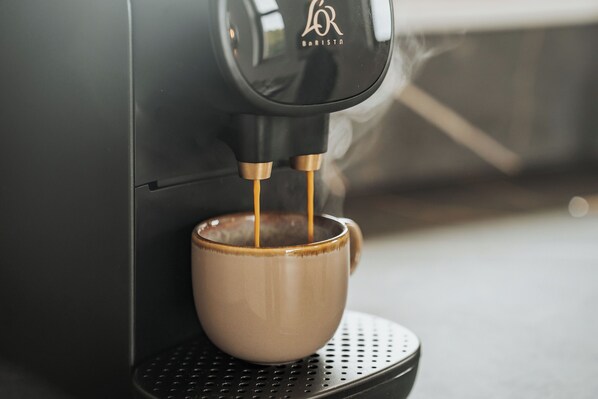 Una cafetera con una taza debajo, conectada a un equipo instalado en la pared.