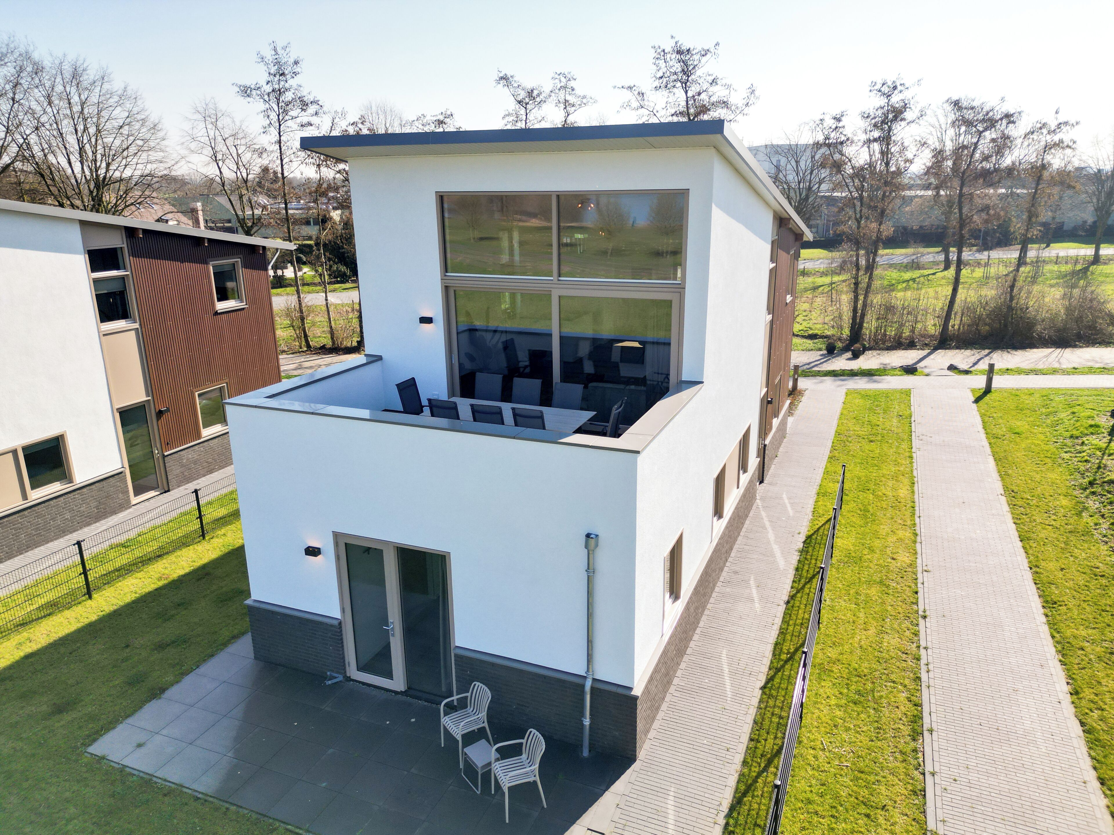 A modern building with a flat roof, large windows, and a patio area with chairs.